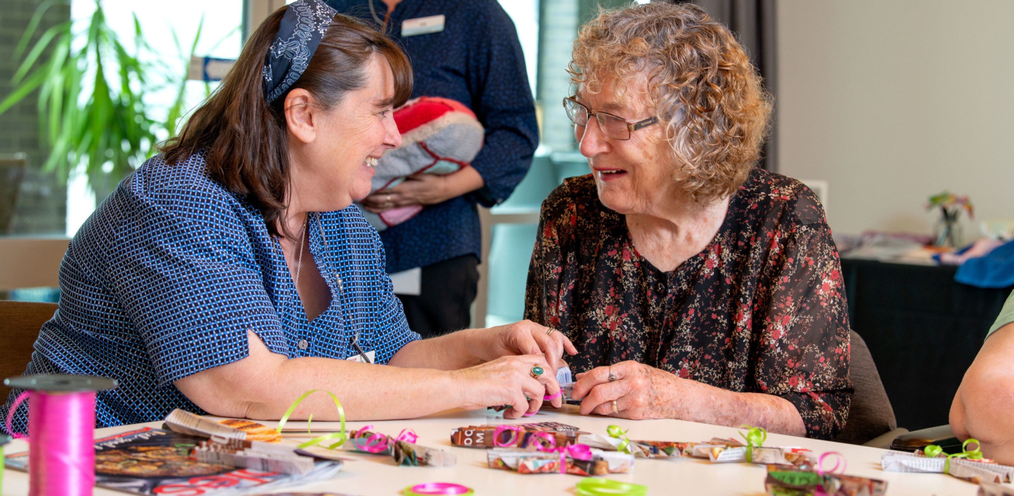 An Eldercare resident and staff member smile at each other as they make crafts together.
