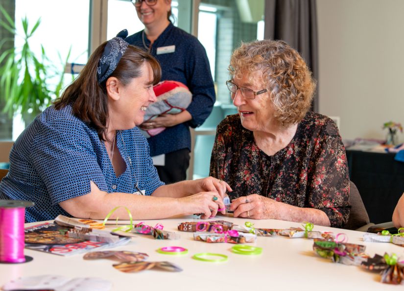 An Eldercare resident and staff member smile at each other as they make crafts together.