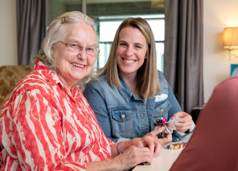 Eldercare Allambi resident and volunteer smiling into the camera as they hold the crafts they are making.