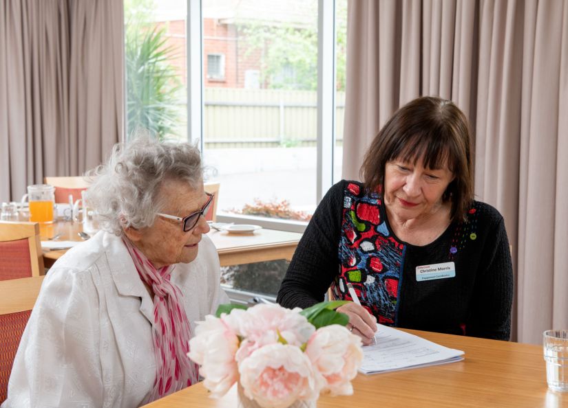 Eldercare Trowbridge House resident and staff member looking down at a form that they are completing together.