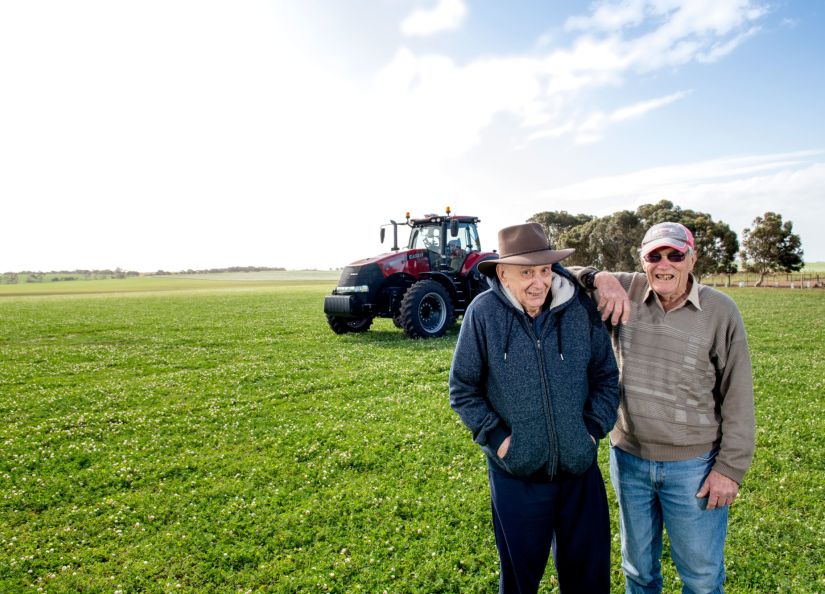 A resident and volunteer from Eldercare The Village smiling at the camera in a field in Maitland against a tractor and blue, cloudy sky.