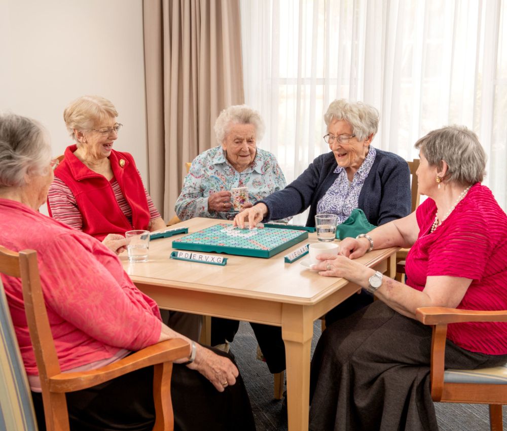 Five Eldercare Cottage Grove residents smiling around a table playing Scrabble.