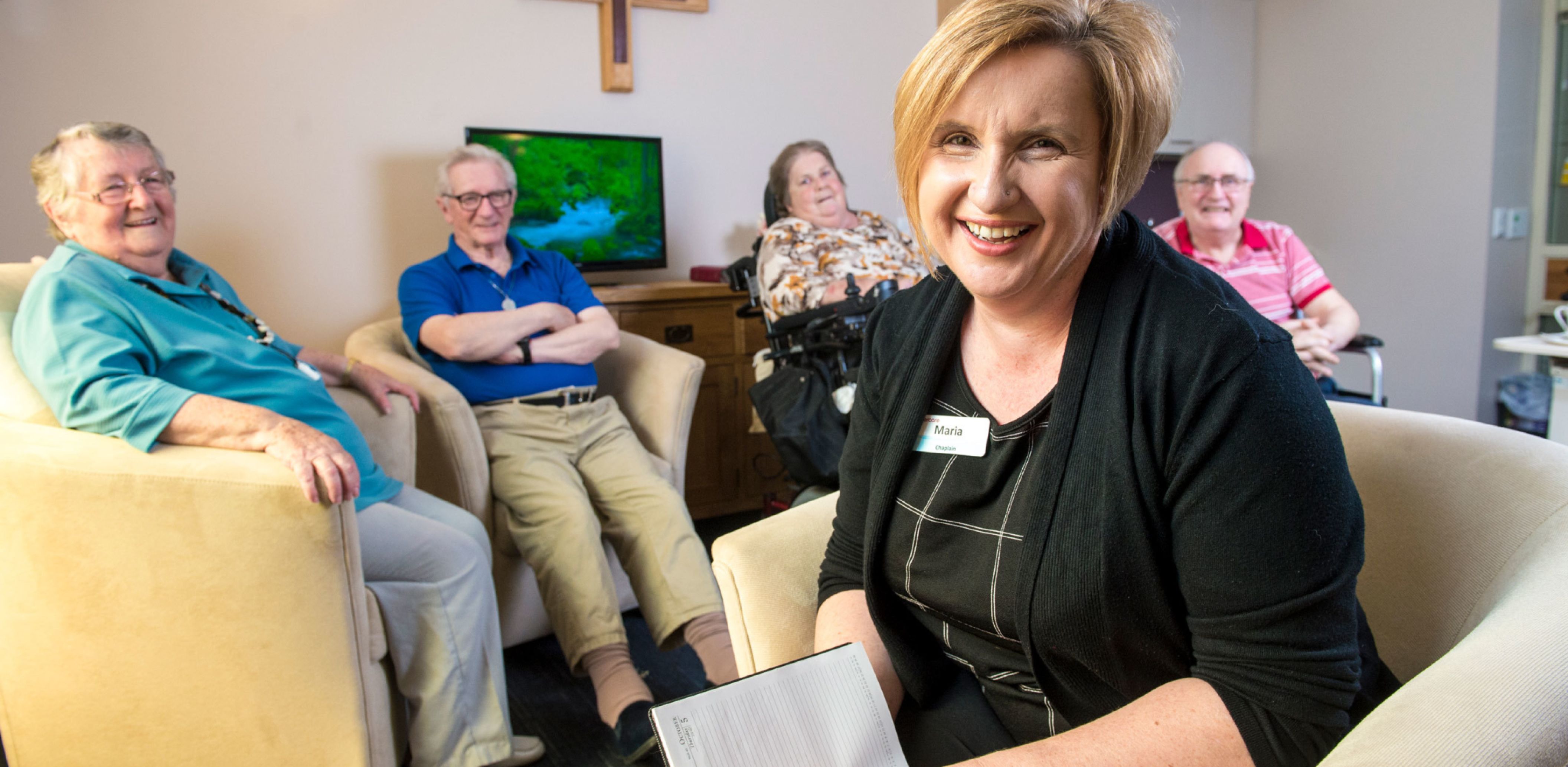 Eldercare Evanston Park Chaplain Maria smiling at the camera with four residents smiling while seated in a group behind her.