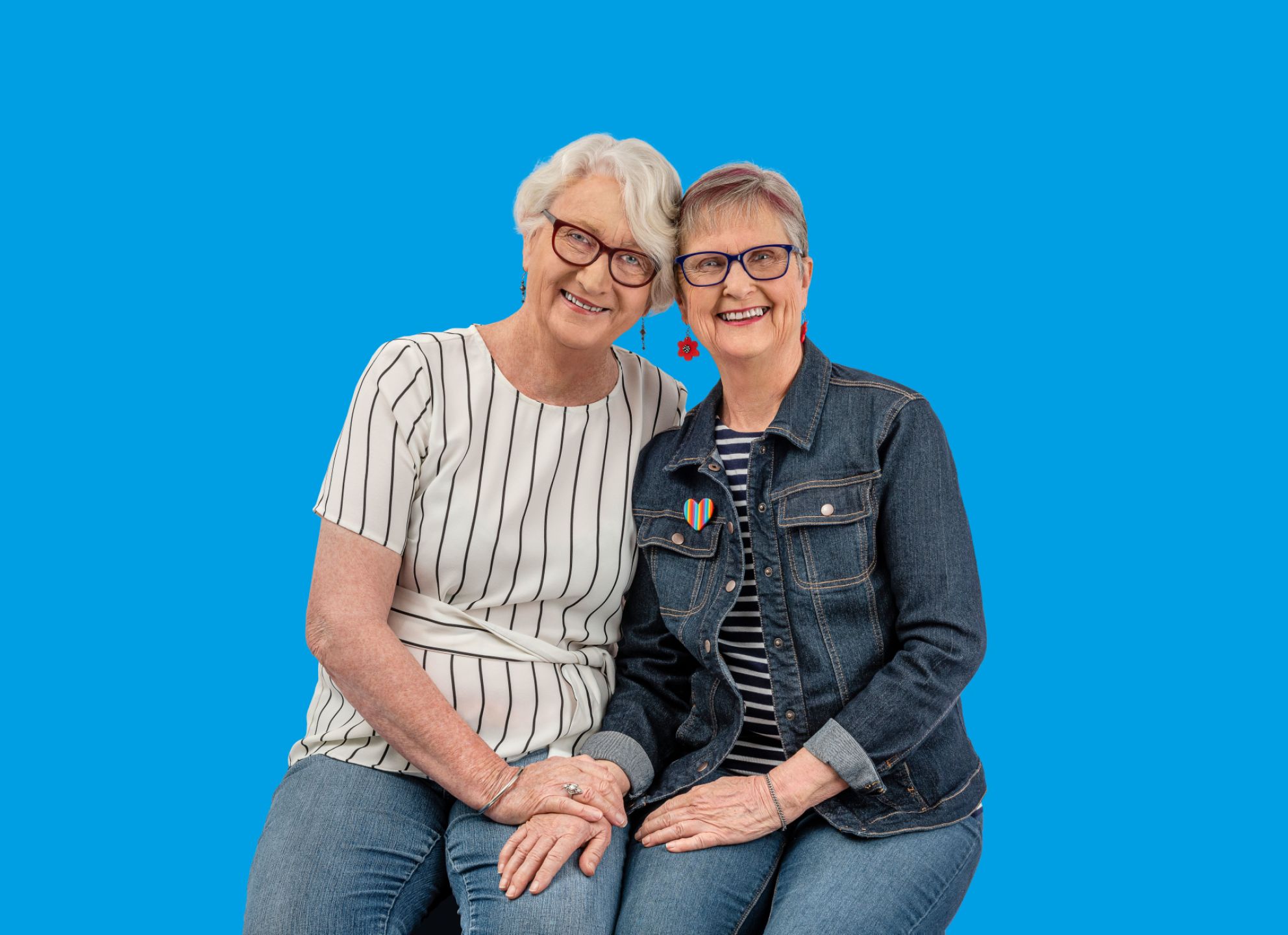 Eldercare LGBTI Advisory Group member Jenny Scott with partner Anthea smiling at the camera in front of a bright blue screen.