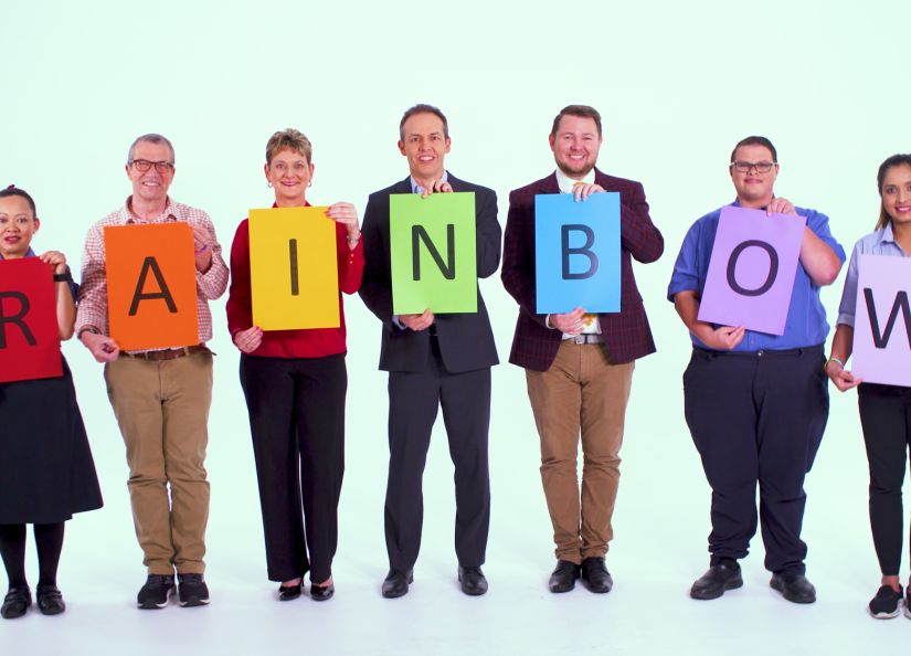 A group of Eldercare staff holding up a single letter on a coloured piece of paper with the word spelling out 'rainbow'.