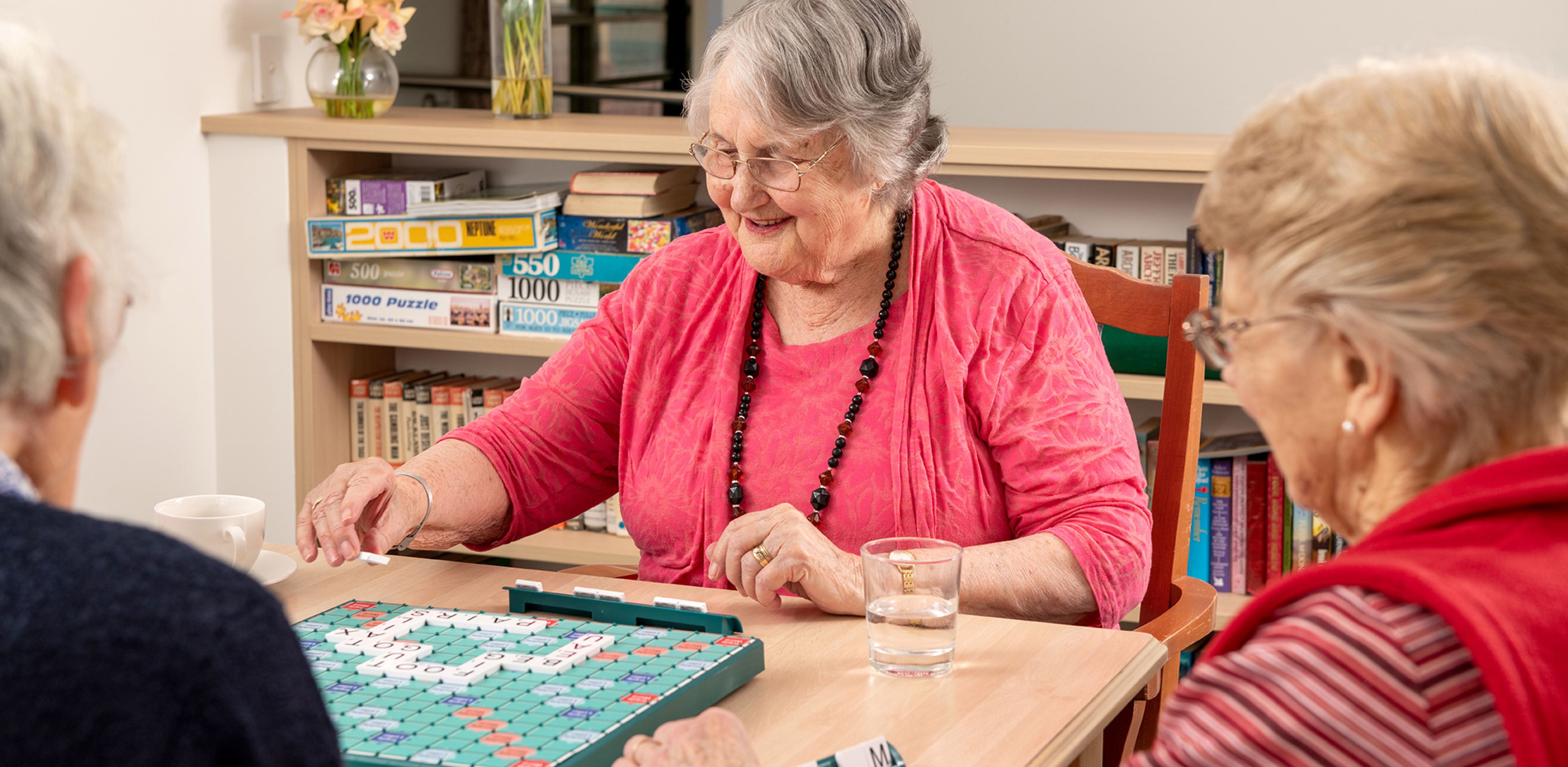 Eldercare Trowbridge House resident smiling and playing scrabble with two friends.