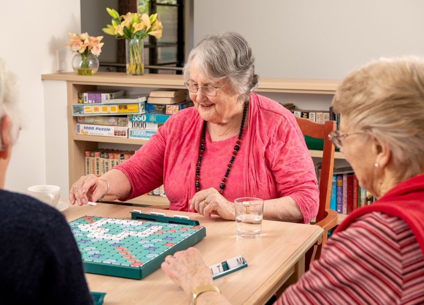 Eldercare Trowbridge House resident smiling and playing scrabble with two friends.