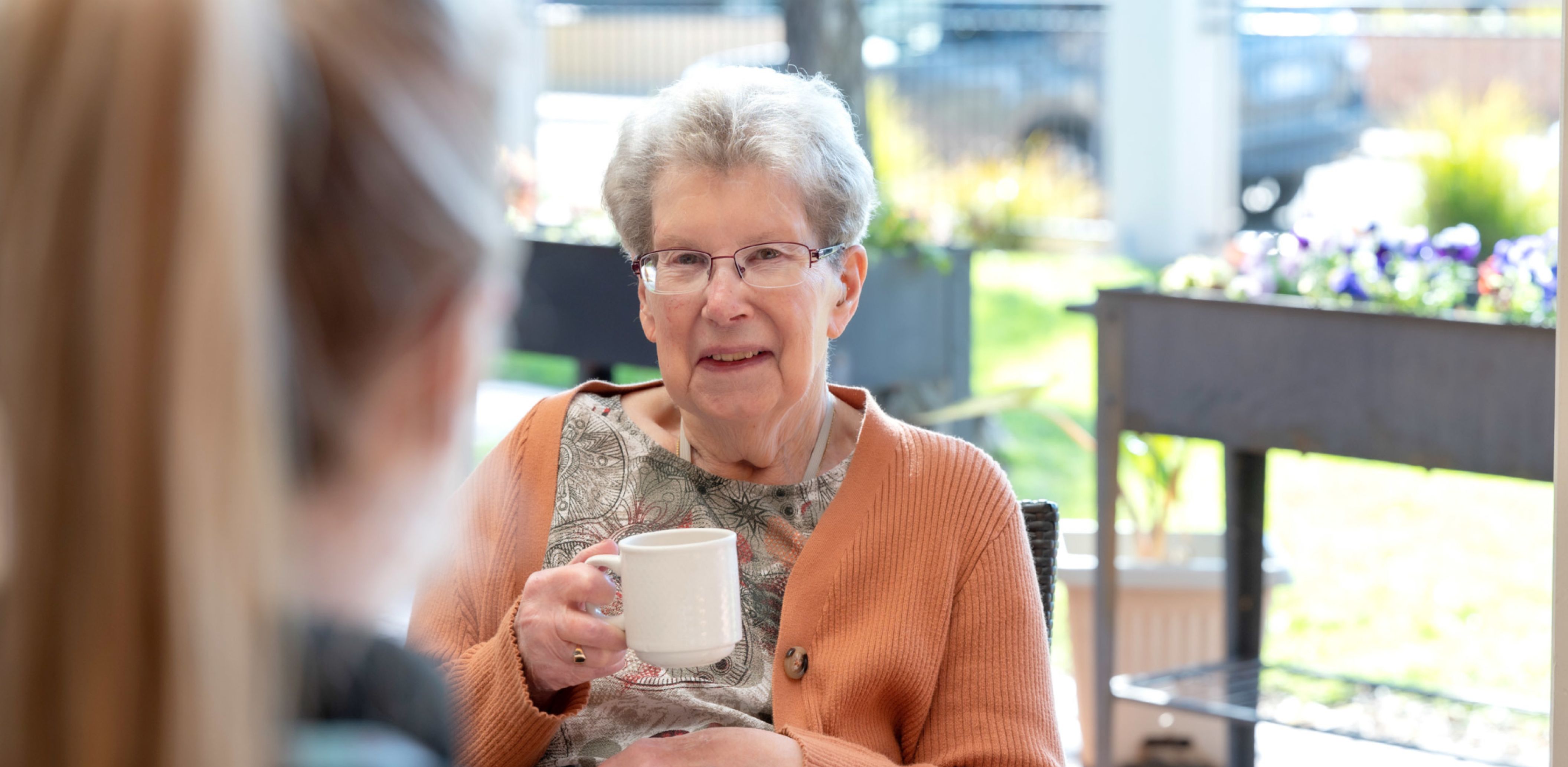A resident is smiling while enjoying a cup of tea in the sun-soaked gardens at an aged care home.