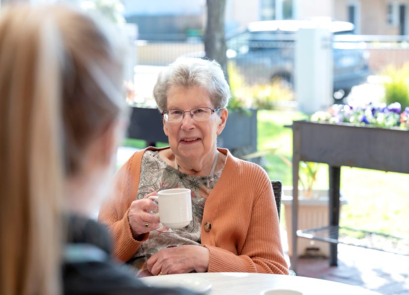 A resident is smiling while enjoying a cup of tea in the sun-soaked gardens at an aged care home.