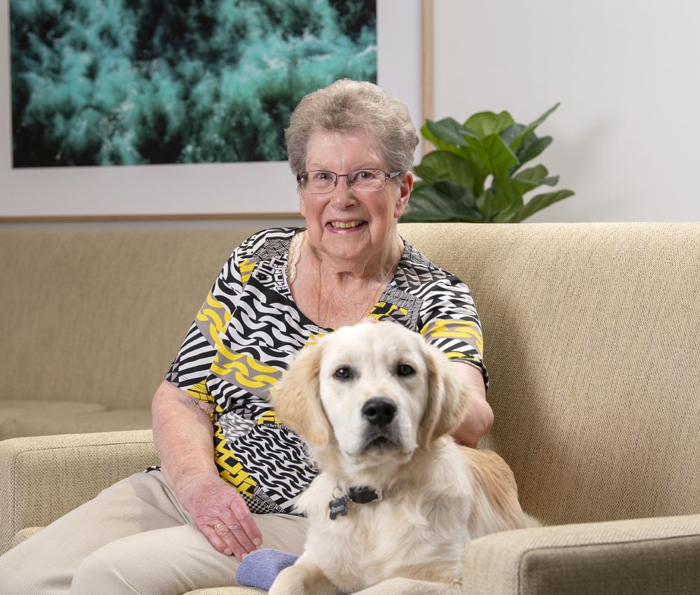 Eldercare aged care resident sitting on a couch and patting a golden retriever puppy