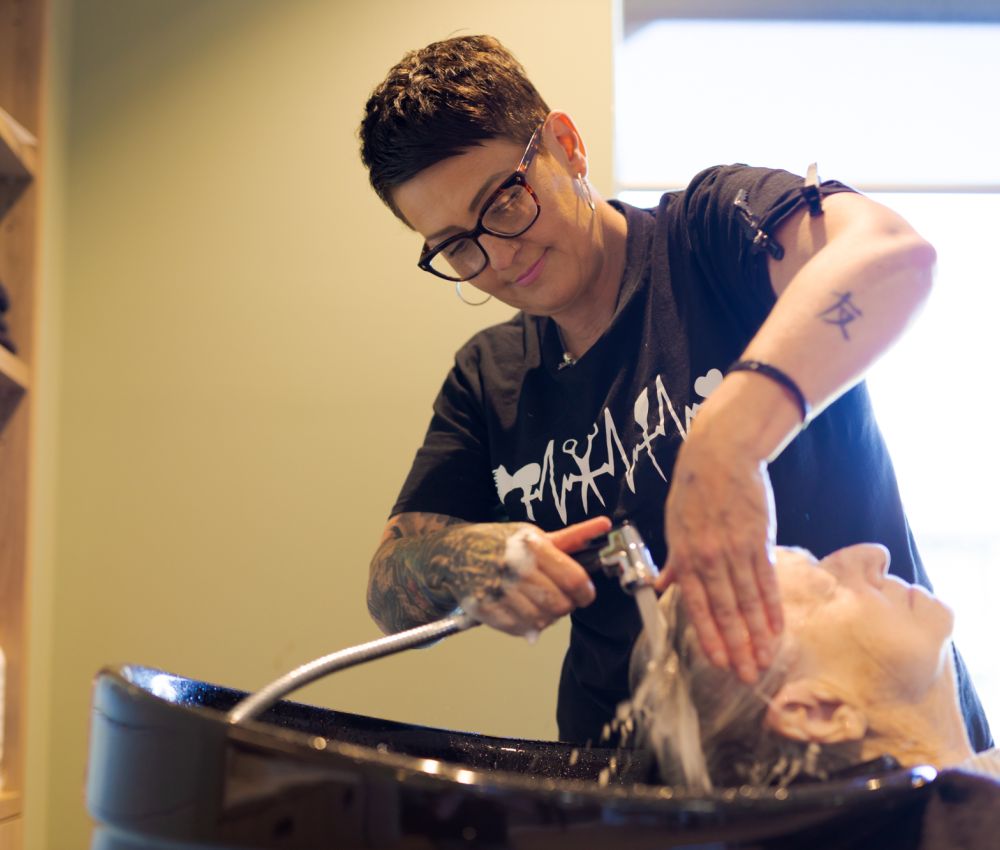 An Eldercare resident sits in the hairdressing salon while having her hair done by a professional hairdresser.