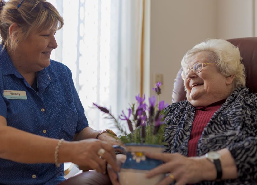 An Eldercare lifestyle support staff member gives a resident a pot filled with lavender.