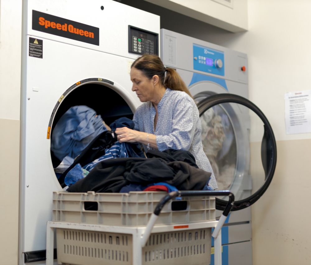 An Eldercare hospitality assistant pulls clothing from the dryer in the laundry.