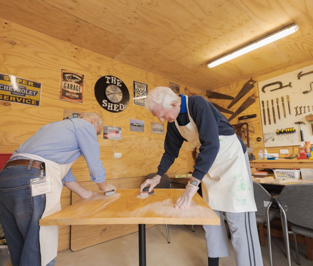 An Eldercare volunteer and resident work together to sand down a table in the workshop at Allambi.