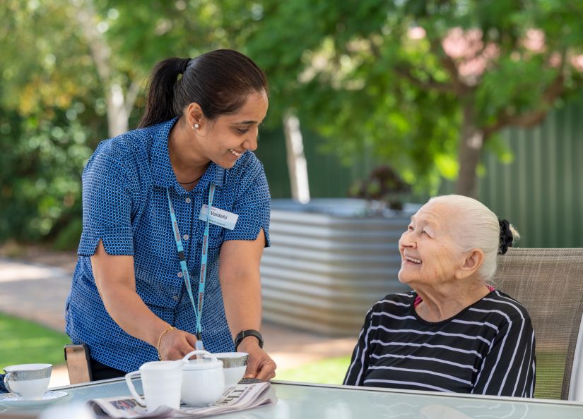 Eldercare staff member bringing a cup of tea to a resident.