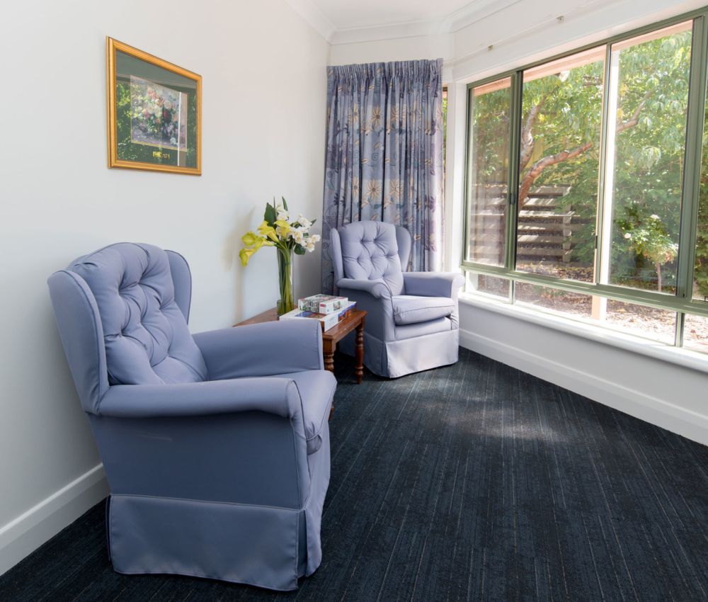 Lounge area at Eldercare Cottage Grove with armchairs and a bunch of flowers in a vase.