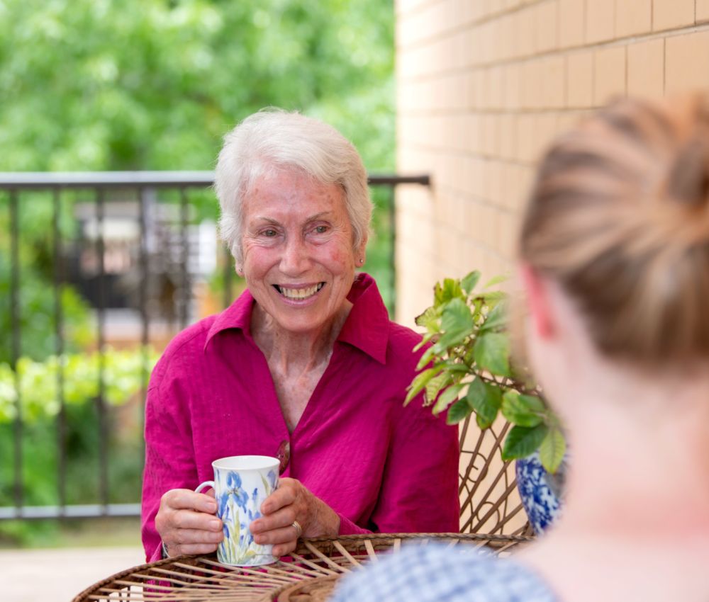 Eldercare College Green Retirement Living resident drinking tea and smiling at an Eldercare staff.